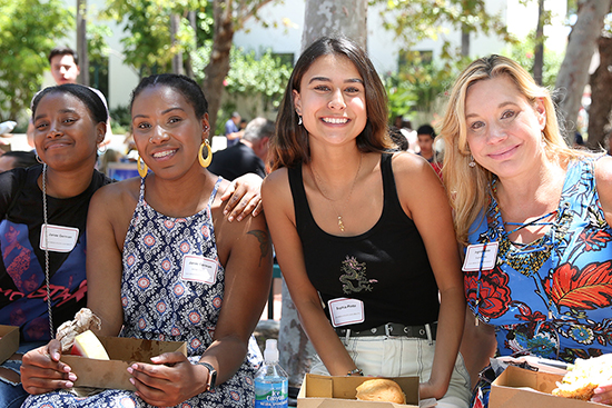 two new students with their moms having lunch at orientation under the trees